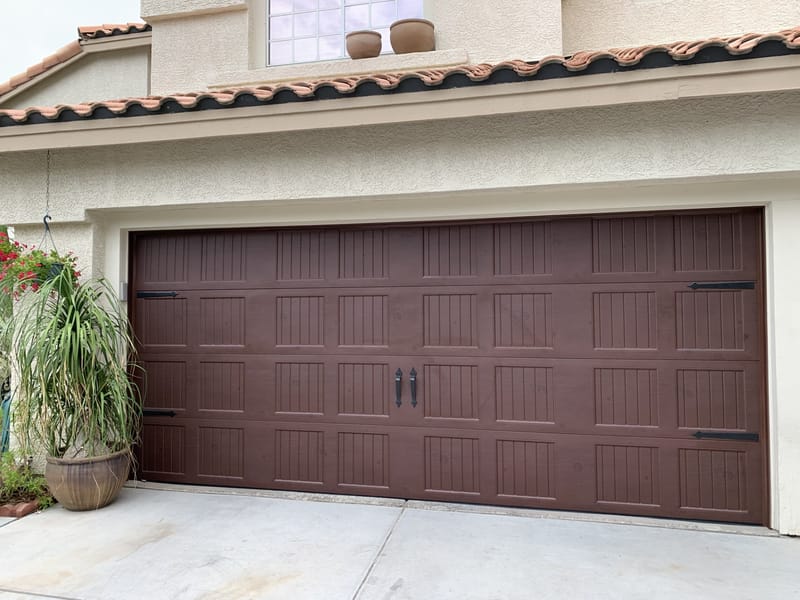 A dark carriage-style double garage door on a stucco home with a tile roof