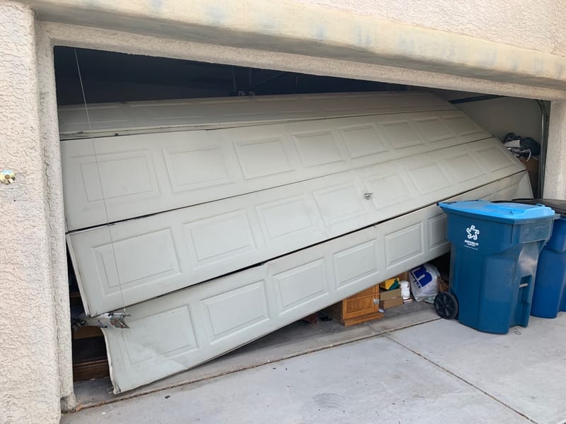 A garage door buckled and hanging out of its track after coming off the rails