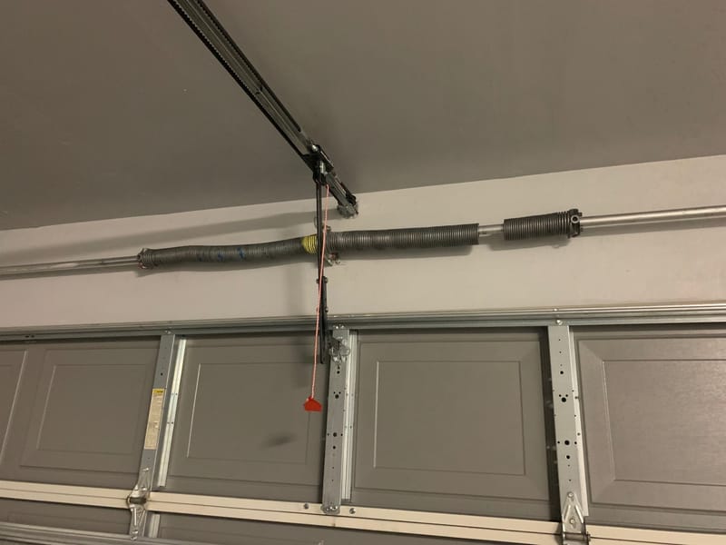 A torsion spring mounted on the shaft above a part-open garage door, seen from inside the garage
